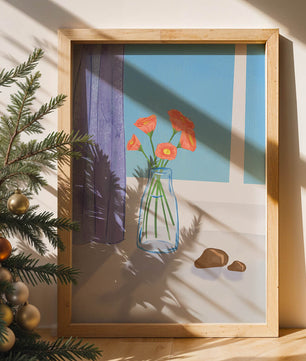 Jarrón con flores naranjas junto a una ventana con cortinas moradas